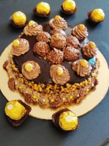 Decorate Ferrero Rocher Cake with whipped cream florets, ferrero chocolates, chopped hazelnuts.